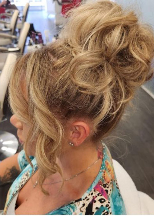 A woman sat in a salon chair with a high bun and curled hair strands at the front.