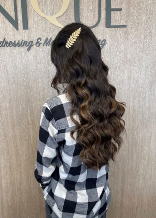 A woman facing away showing her long curled brunette hair with gold leaf hair clips.