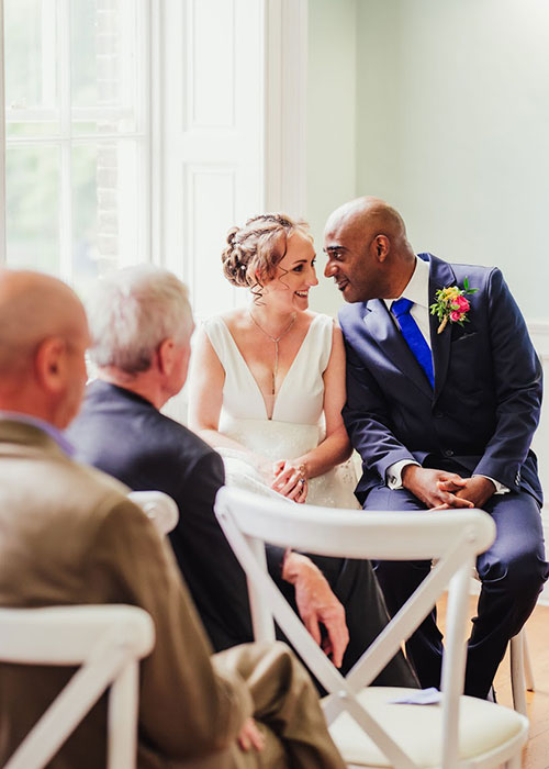 Bride and groom sat next to each other and the groom is looking at the bride.
