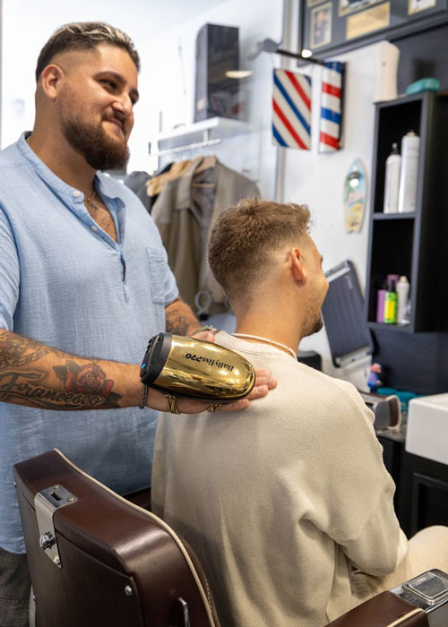 Barber using a hand held massage machine on a man in the barbers chair.