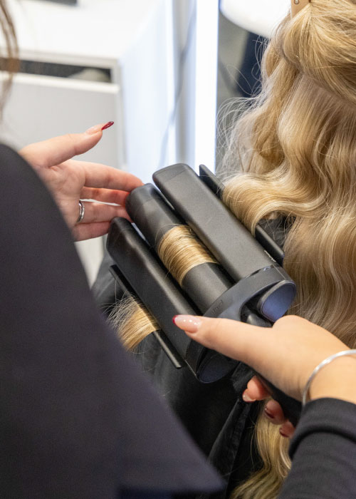 A hairstylist is curling a woman's hair using a large curling wand.