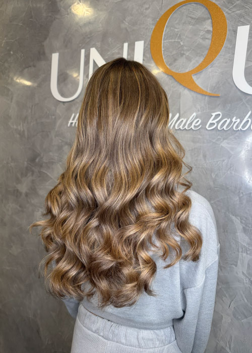 A girl in the Unique Hairdressing salon has long curly hair with blonde highlights.