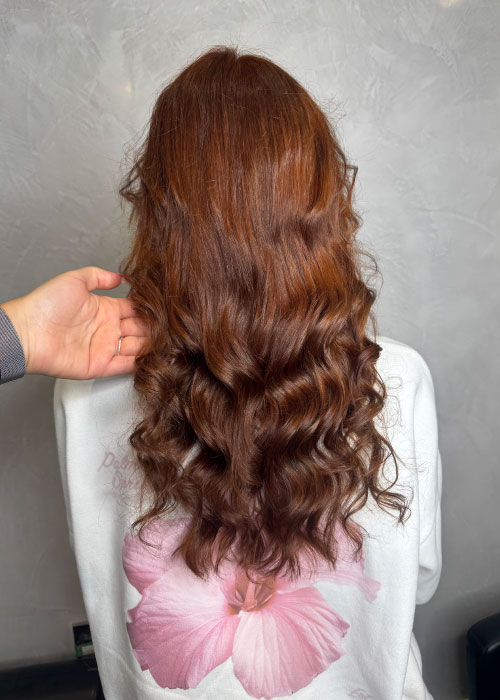 A girl with long red hair styled in long wavy curls at Unique Hairdressing.