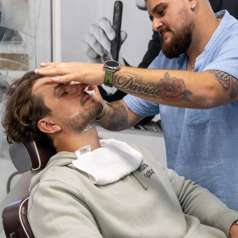 A man in a barbers chair is getting his beard groomed by a barber at Unique.