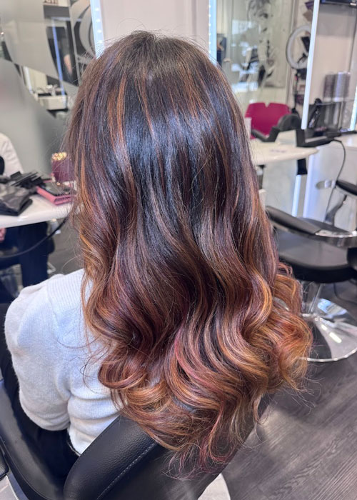 A girl with light red lowlights is sat in a salon chair at Unique Hairdressing.
