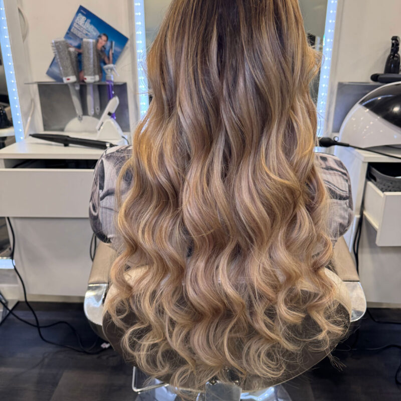 A girl sat in a salon chair at Unique Hairdressing with curly blonde hair extensions.