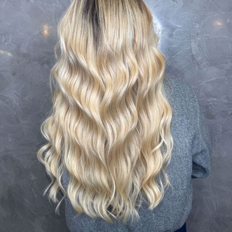 A girl's long, blonde, wavy hair extensions from Unique Hairdressing in Bishop's Stortforfd.