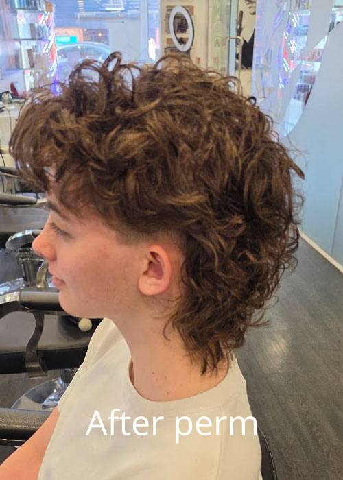 Someone sat in a salon chair with a curly mullet haircut.